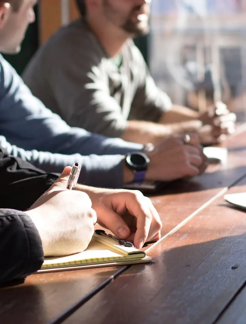 A person takes notes at a meeting happening around a table